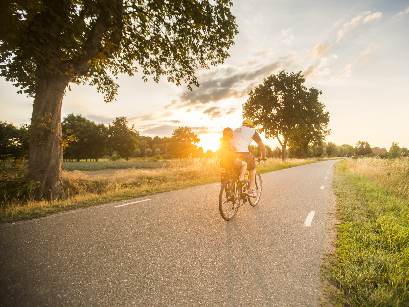 Man op fiets met kind tijdens zonsondergang 
